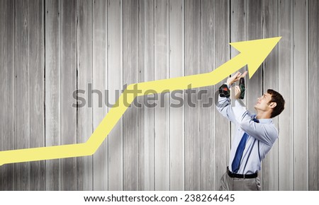 Young businessman using drill to fix growing arrow