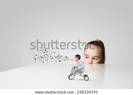 Little girl looking at boy riding three wheeled bicycle