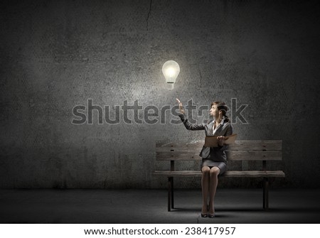 Young smiling businesswoman sitting on bench with book on knees
