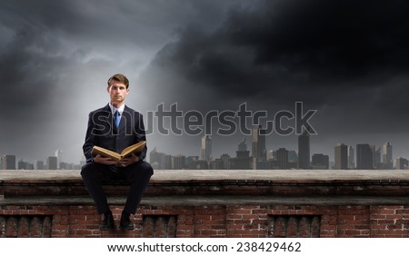 Young businessman sitting on building top with book