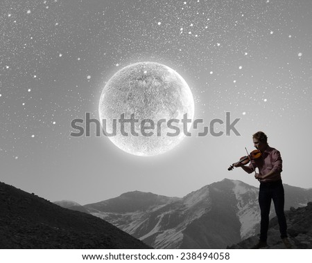 Young man playing violin at night under moon light