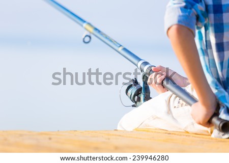 Close-up of hands of a boy with a fishing rod that is fishing on the pier
