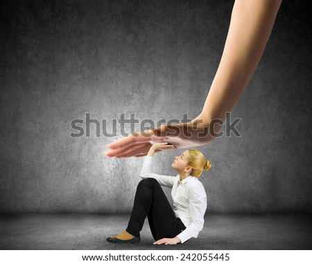 Young woman sitting on floor and pressed by huge hand