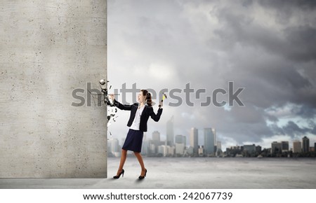 Young businesswoman hitting nail in wall with hammer
