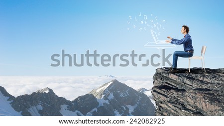 Young man sitting in chair on top of rock and using laptop