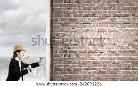 Young businesswoman hitting nail in wall with hammer