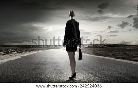 Back view of businesswoman standing on road and looking far away
