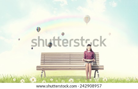 Young woman sitting on bench and reading book