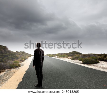 Back view of businessman standing on road and looking far away