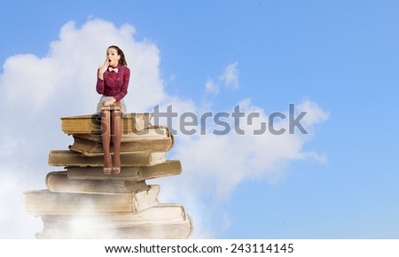 Young woman sitting on pile of books with book in hands