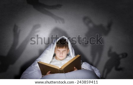 Little cute boy sitting in bed under blanket with book