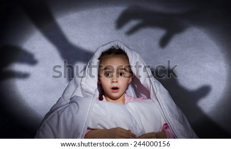 Cute scared girl sitting in bed under blanket