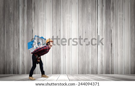 Young builder man in hardhat carrying house model on back