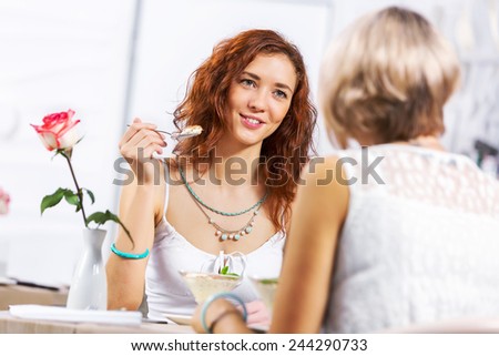 Two young pretty women sitting at cafe and eating dessert