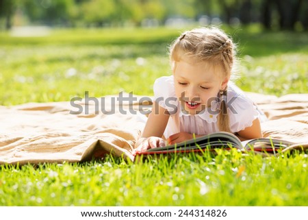 Little cute girl in summer park reading book