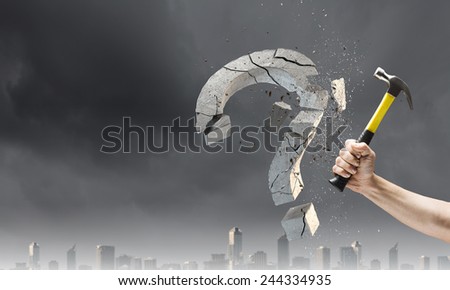 Close up of hammer in human hand breaking stone question mark
