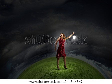 Young attractive woman in red dress with lantern walking in darkness