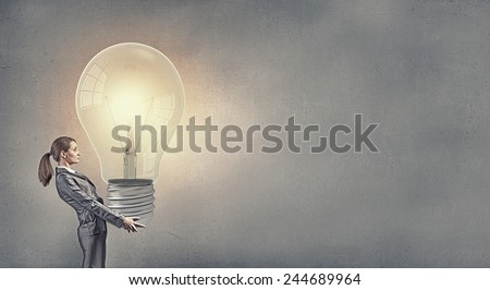Young businesswoman carrying big light bulb in hands