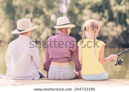 Rear view of three children sitting at bank and fishing