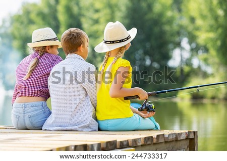 Rear view of three children sitting at bank and fishing