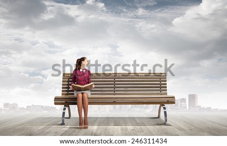 Young woman sitting on bench and reading book