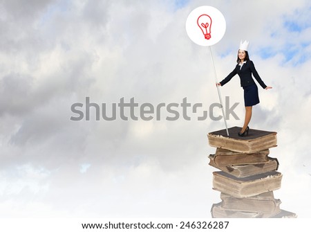 Young businesswoman in paper crown standing on pile of books