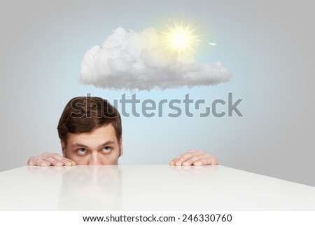 Young businessman looking from under table at sun behind cloud