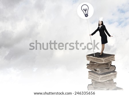 Young businesswoman in paper crown standing on book