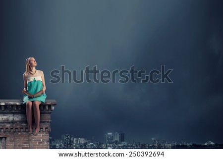 Young pretty girl sitting on building top with book