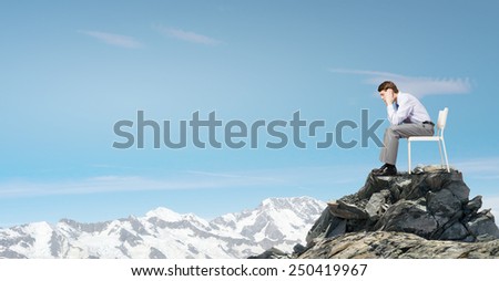 Troubled businessman sitting in chair on top of mountain