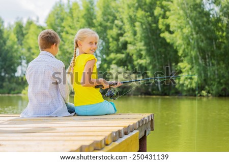 Rear view of two children sitting at bank and fishing
