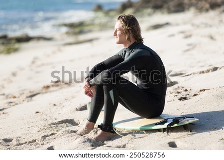 A young man sitting on his surfboard on the sand