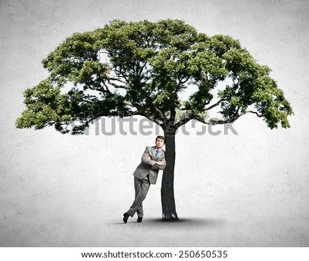 Young relaxed businessman leaning on green tree