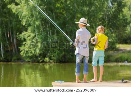 Rear view of two children standing at bank and fishing