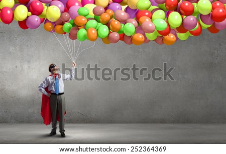 Young confident super guy in mask and cape with bunch of balloons