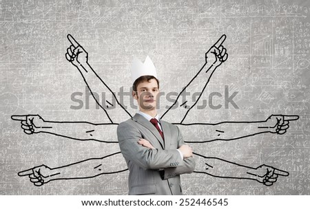 Young businessman in paper crown and many hands around him