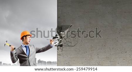 Businessman in helmet hammering nail in brick wall