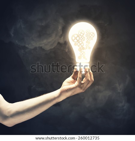 Close up of human hand holding light bulb with gears inside