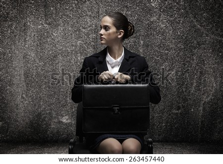 Upset businesswoman sitting on chair with suitcase in hands
