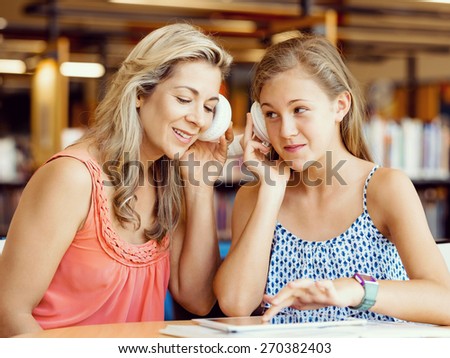 A teenage girl with headphones sitting in a library with her mum