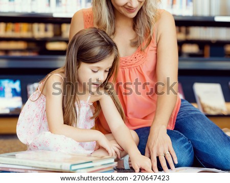 Little girls with their mother reading books in library