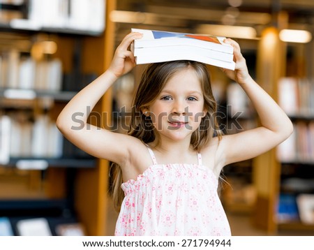 Little girl with a book on top of her head in library