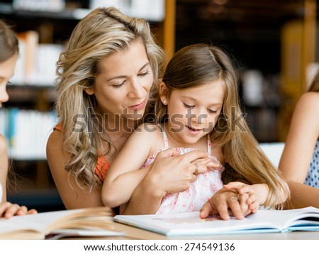 Little girls with their mother reading books in library