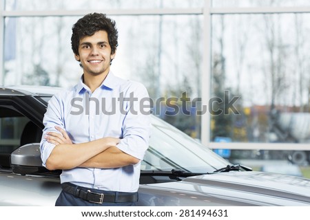 Handsome young man standing besides car in showroom