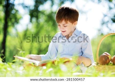 Cute boy in summer park sitting on blanket and reading book