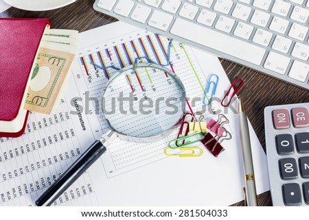 Magnifing glass and documents with analytics data lying on table
