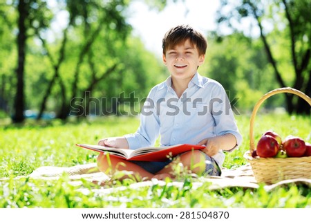 Cute boy in summer park sitting on blanket and reading book