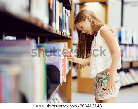 Little girl picking a book in public library