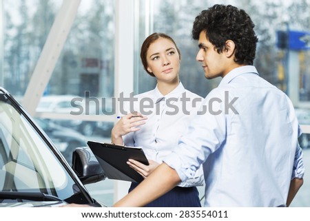 Young woman dealer in auto salon presenting car to customer