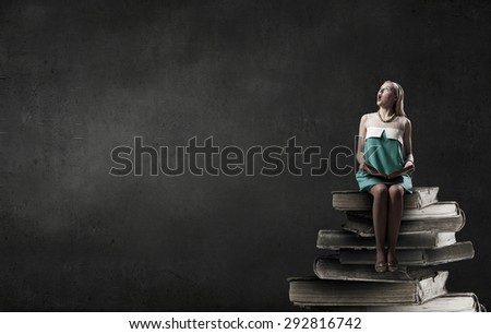 Young beautiful lady sitting on pile of old books
